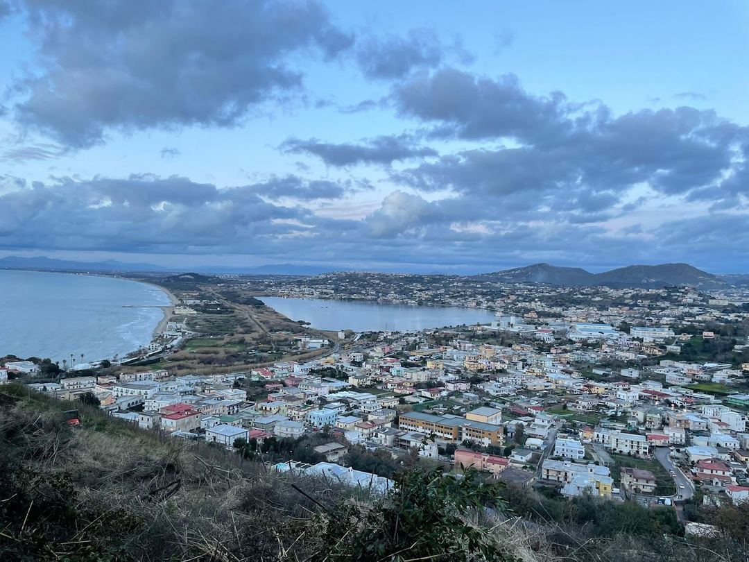 Aerial view of a coastal town with colorful buildings overlooking a crescent bay and surrounding hills during golden hour.