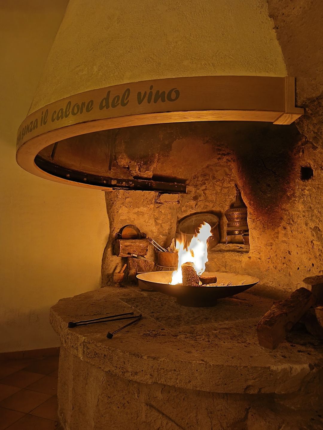 A traditional rustic fireplace with an active fire and a wooden barrel labeled 'Aroma il valore del vino' mounted above it.