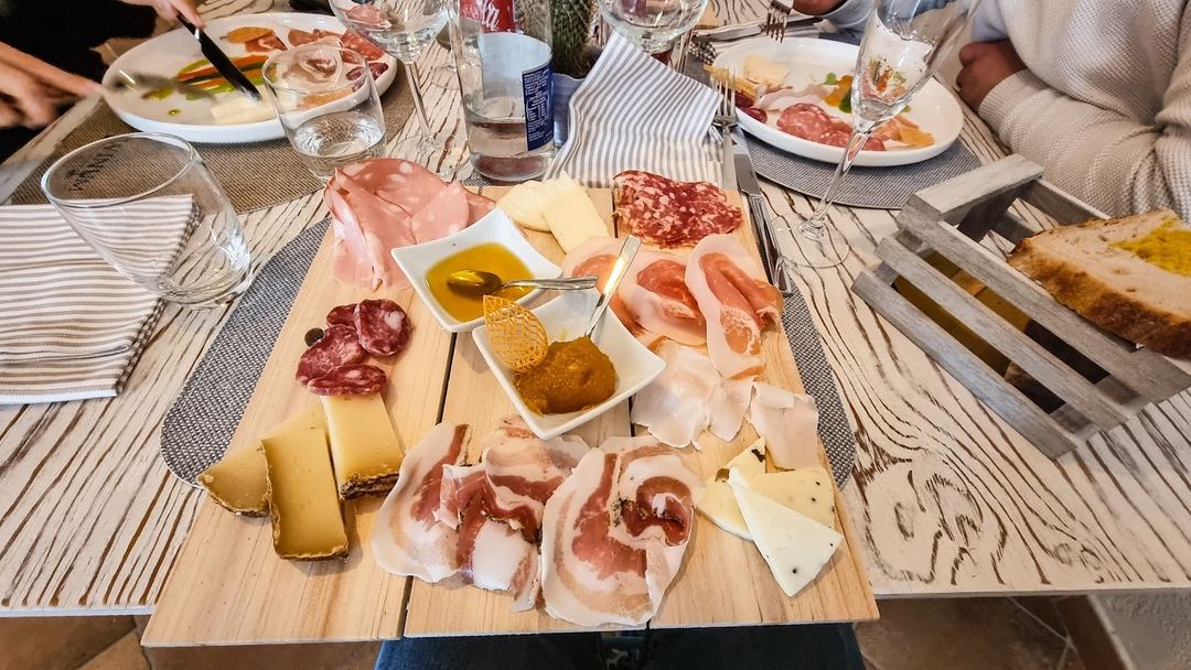 A charcuterie and cheese board featuring cured meats, aged cheeses, and spreads served at a dining table with guests.