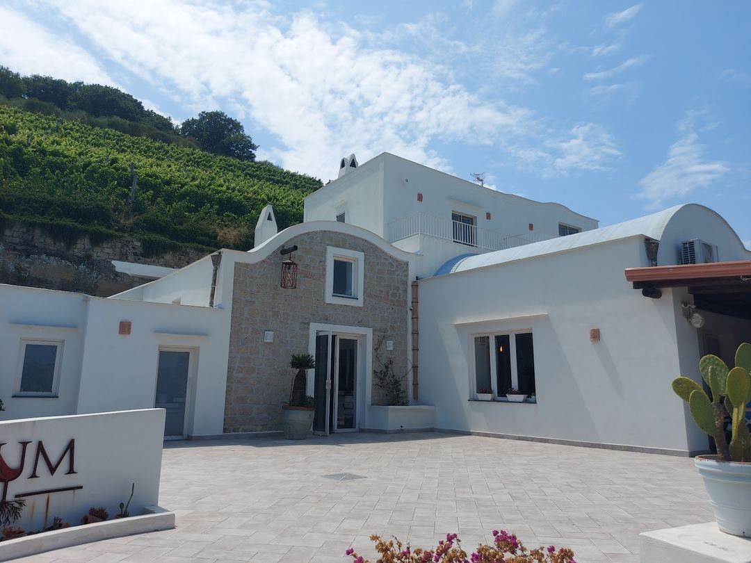 The whitewashed Mediterranean-style main building of Lavinum hotel features curved architectural elements, stone accents, and a spacious courtyard with flowering plants.