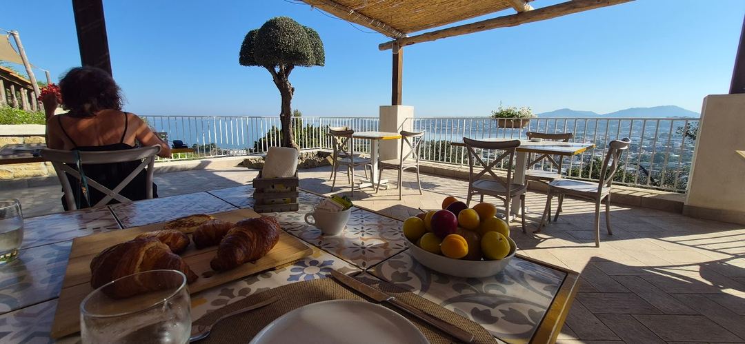 A scenic terrace breakfast setup at Lavinum with panoramic views of mountains and coastal landscape under clear skies.